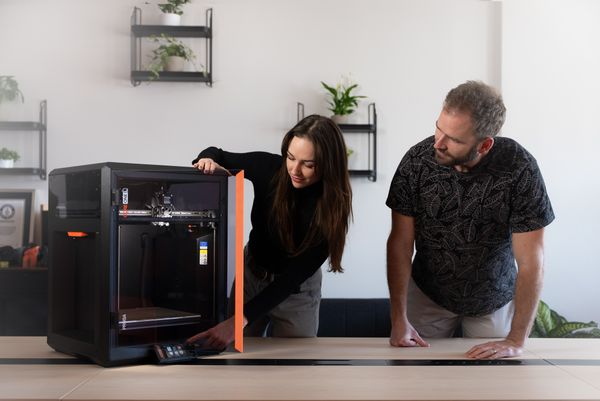 A woman recommending the Prusa CORE One L 3D printer to a male colleague.